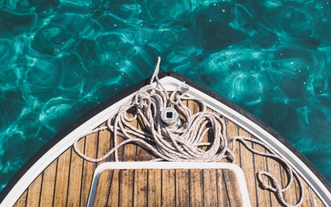 Edge of a boat with some ropes with sparkling blue water in the background