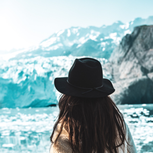 Back of girl wearing a black hat looking towards snowy mountains 